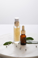 Bottles of cosmetic oil with leaves and decorative balls on round stand isolated on grey