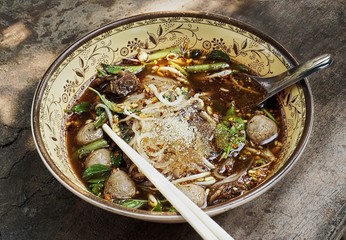 Thai traditional noodle soup with meat balls chili and sugar on rough wooden surface outdoors