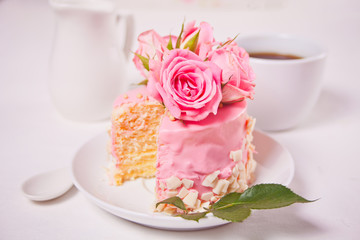 Mini small cake with pink glaze, beautiful roses, cup of coffee on the white table.