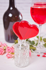 Red heart shape candies with glasses of red grape wine with bottle and roses on the background
