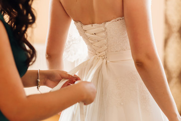 bridesmaid tying bow on wedding dress. corset. close up
