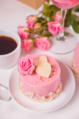 Mini cake with pink glaze, beautiful roses, cup of coffee, glass of pink wine on the white table.