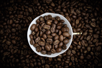 White cup of coffee filled with coffee beans. Vignette. Top view.