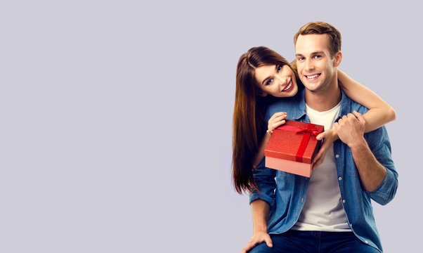 Love, relationship, dating, flirting, lovers concept - happy smiling amorous couple opening gift box. Over grey background. Copy space for some text.