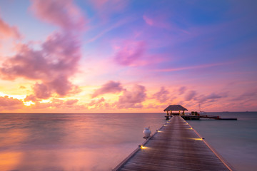 Sunset on Maldives island, luxury water villas resort and wooden pier. Beautiful sky and clouds and beach background for summer vacation holiday and travel concept. Paradise sunset landscape
