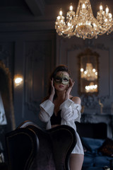 Fototapeta na wymiar Beautiful sexy girl in carnival mask and white shirt in a classic interior..