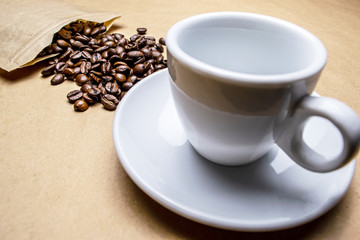 Coffee beans sprinkled from the packaging and a white cup on a beige background,