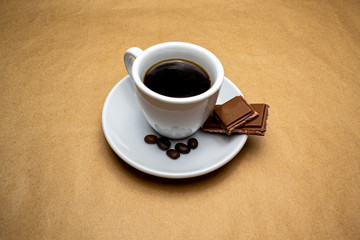 Coffee in a white cup on a saucer slice chocolate bar beige background
