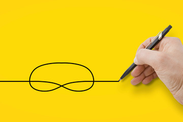 Hand holding a black pencil drawing a knot on yellow background