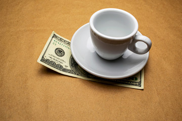 One hundred dollars under an empty white cup on a beige background
