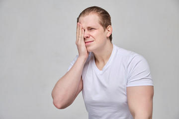 A man in a white T-shirt massages his eye - terrible pain due to inflammation.