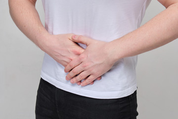 A man in a white T-shirt massages his stomach due to severe pain in the pancreas, intestine.