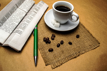 White cup with coffee on a napkin, green ballpoint pen, newspaper, on a beige background