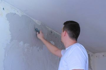 Plasterer man spackling wall with putty plaster aligning wall. Finishing construction renovation works in apartment. Worker builder making overhaul in flat applying plaster on wall using trowel.