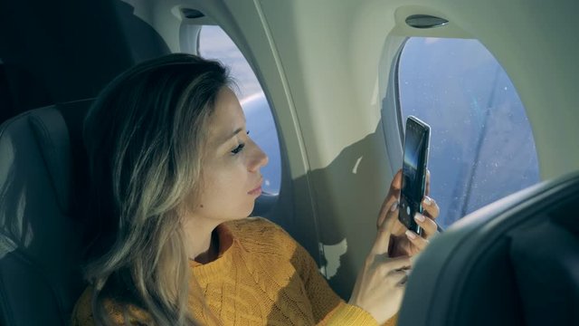 A woman is taking pictures with her cellphone during her flight