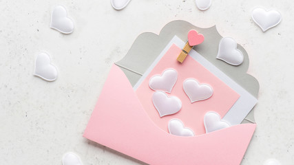 Pink envelope full of decorative hearts on white stone background. Love concept. Romantic congratulation on Valentine's Day.