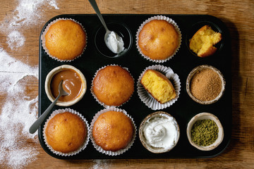 Homemade citrus oranges or clementines sweet muffins cakes in baked tray with flour, ingredients and different topping above over wooden cutting board as background. Flat lay, space