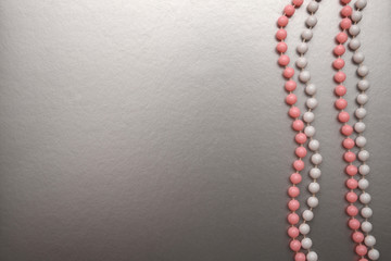 White and pink beads on a silver background. Copy space, flat lay.