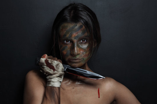 Young Woman With Camouflage Face Paint And Knife In Her Hand