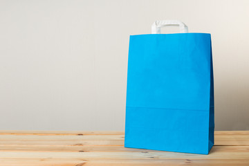 An empty paper bag with handles for shopping, on the front right side of a table in light wood with...