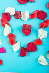 Heart of rose petals on a blue background and a heart-shaped box with a pendant.