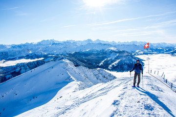Fototapeta na wymiar mountaineer against swiss alps mountain panorama in winter. hiker in front of snowy mountain panorama, blue sky swiss national flag