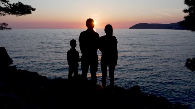 Silhouettes of a young family standing near the sea at sunset.