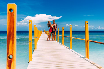 A happy couple on vacation strolling along a wooden pier above the tropical, turquoise ocean in...