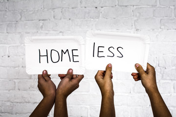 Two pairs of children's hands hold two cardboard signs. On the background of a white brick wall. ...