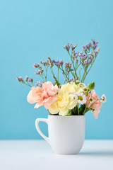 Beautiful little flowers bouquet in white mug on blue background