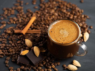 A glass Cup of coffee with grated roasted almonds on a concrete table and scattered roasted grains