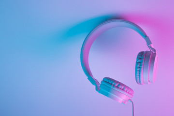 Retro 90s style photo of white stylish wireless headphone in neon lights. Music concept.