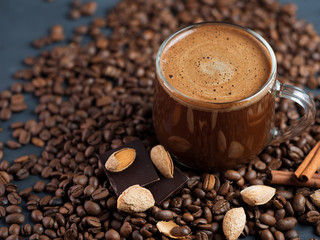 A glass Cup of coffee with grated roasted almonds on a concrete table and scattered roasted grains