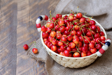 Wicker basket full of ripe sweet cherry with water drops. Rustic wooden background with copy space...