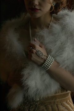 Close up view of young adult caucasian model wearing 1920s style vintage clothes holding her furry collar. Vintage fashion accessories. Dramatic lighting indoors portrait.