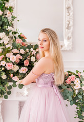 Beautiful romantic young woman with natural makeup posing against a background of flowers. The girl is blonde with a clean look and a beautiful smile.Close-up portrait. Perfume and cosmetic concept