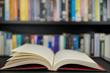 An open book on a working table and a bookshelf in background