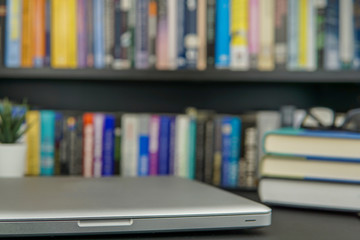 Laptop computer on a working table and a bookshelf in background