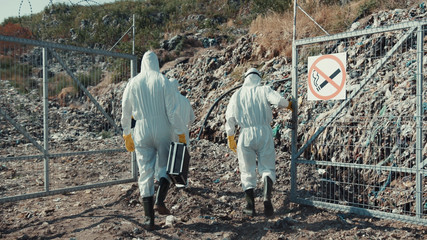 Men ecologists in chemical protection walking on trash dump inspecting land and industrial waste....