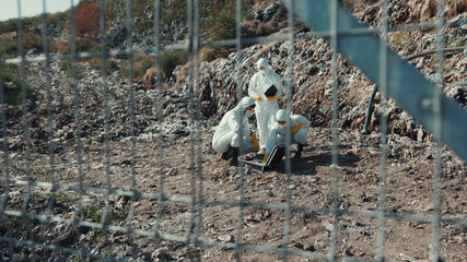 View of ecology specialists collecting samples in test tubes working in polluted stinky disposal site. Environment in danger.
