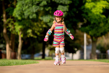 little blonde girl in colorful clothes rides on roller skates in the summer in the Park
