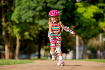 little blonde girl in colorful clothes rides on roller skates in the summer in the Park