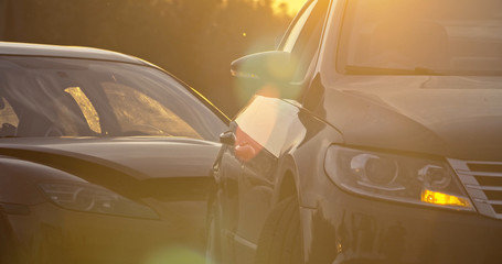 Car accident in the city. View of two modern cars crashed standing stuck on the road at sunset. Traffic collision.