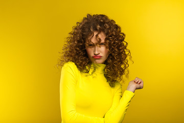 Portrait of young beautiful women with curly hair and suspicious skeptical expression. Nice girl with wavy hairstyle and bright make up isolated over yellow background. Yellow lifestyle. Copy space.
