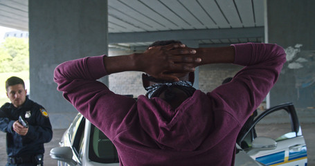 Close-up black man perpetrator wearing mask raising his hands by police order. Police officers on...