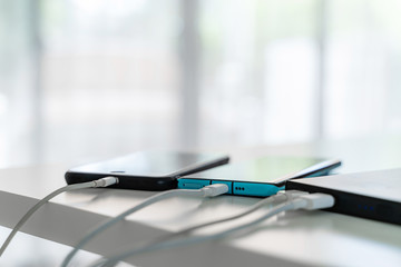 Mobile phone connected to charger power bank on white table.