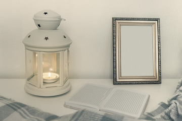 Winter still life interior details, lantern with burning candle, open book and a photo frame on the table