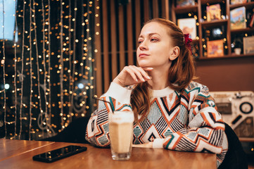 Fototapeta premium Attractive young woman sits at a table in a cafe with a cup of coffee