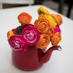 Pink and yellow artificial Ranunculales in red milkman decorate a table in an outdoor cafe
