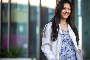 Candid lifestyle portrait of a female medical professional in a white coat walking outside workplace